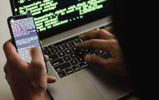 Free Unrecognizable hacker with smartphone typing on laptop at desk Stock Photo